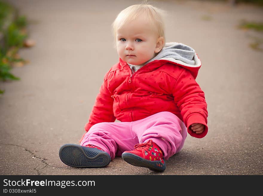 Young adorable baby sit on asphalt road and look to camera