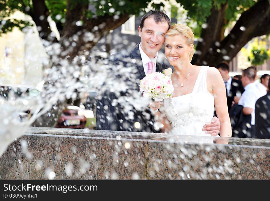 Bride and groom stand near fountain