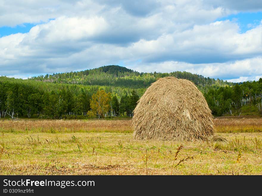 Blue sky and clouds over green hills with haystack. Transbaikalian landscape