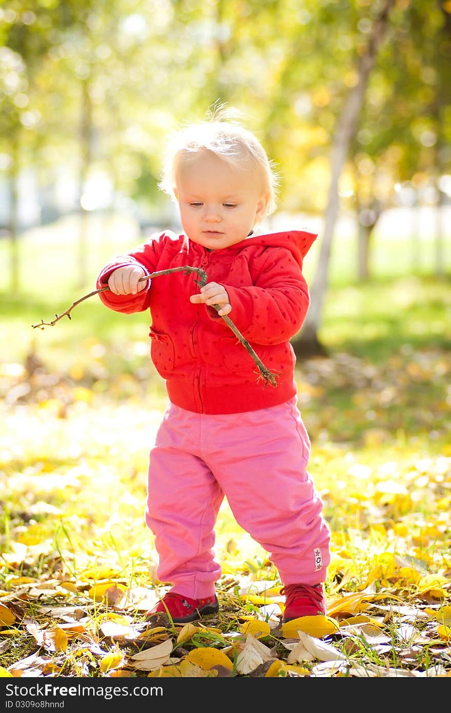 Young cheerful baby play with wooden brench under trees in park