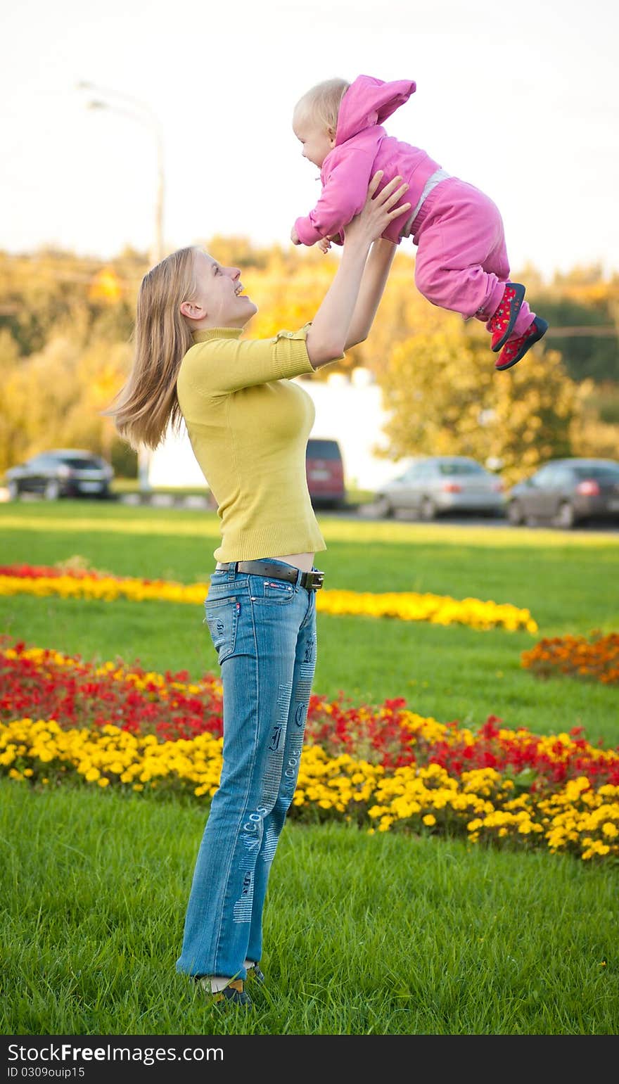 Young adorable woman stay on green grass and play with cute baby on hands in air. Young adorable woman stay on green grass and play with cute baby on hands in air