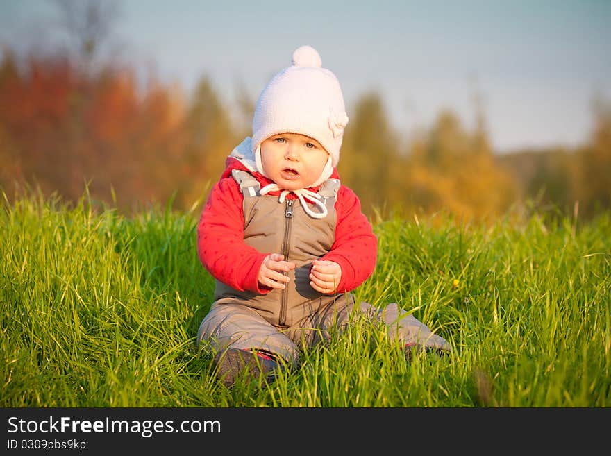 Young adorable baby sit near top of hill and play with green grass