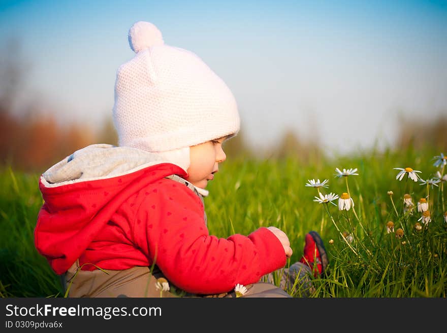 Adorable baby sit on hill and touch flowers