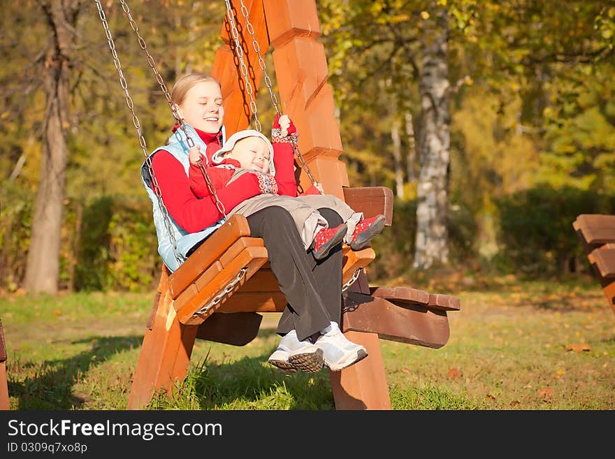 Young adorable mother swinging with dughter in autumn park