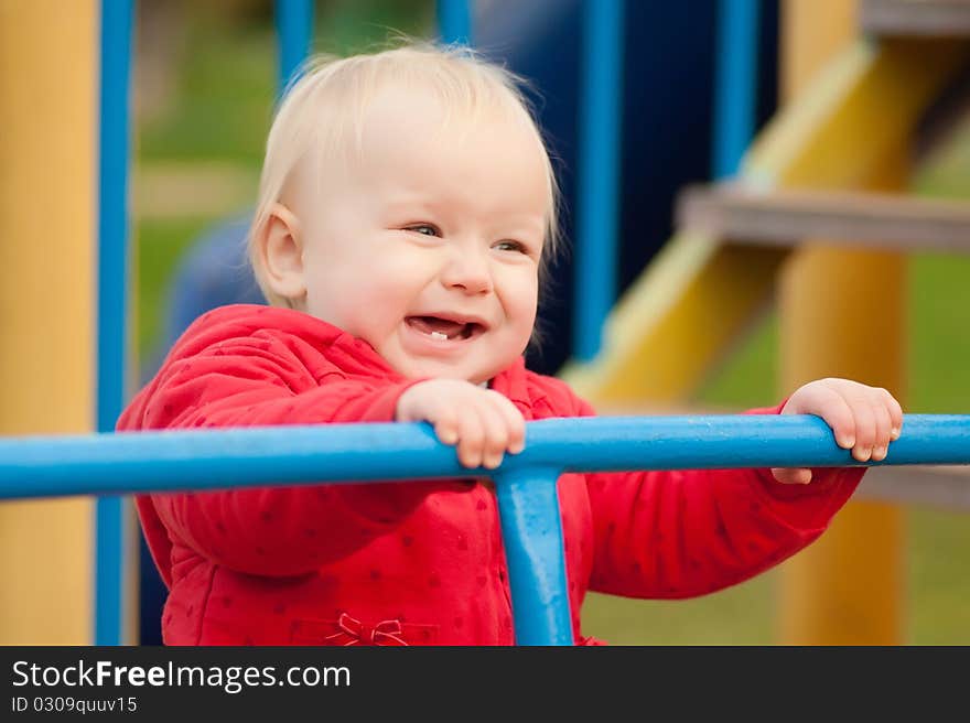 Cute cheerful toddler girl holding the rails on playground and smile. Cute cheerful toddler girl holding the rails on playground and smile