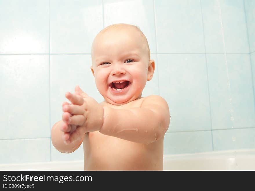 Cute cheerful baby slapping on the water in bath