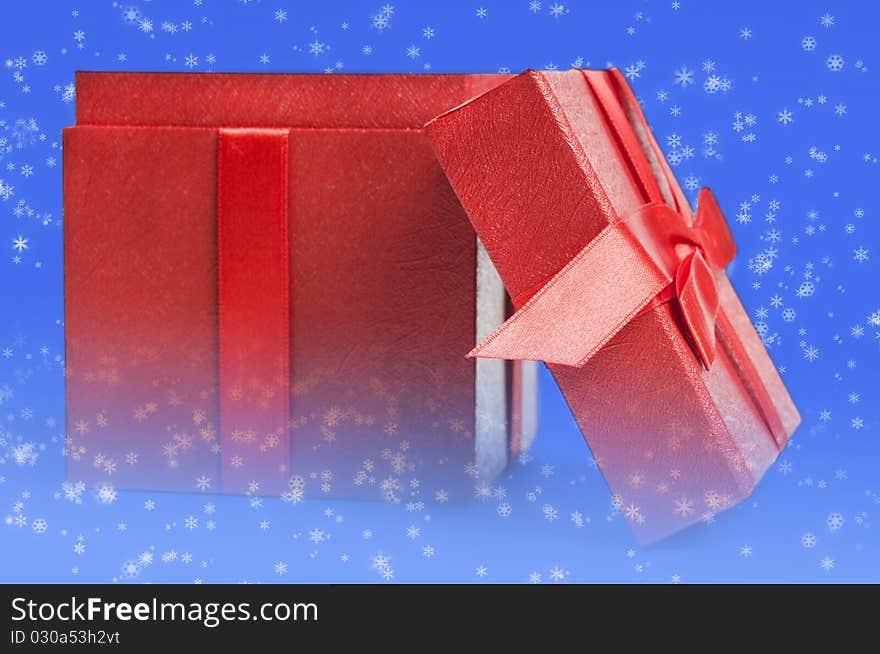 Christma spresent in form of a red box with ribbon melted with lue background with white snowflakes. Christma spresent in form of a red box with ribbon melted with lue background with white snowflakes