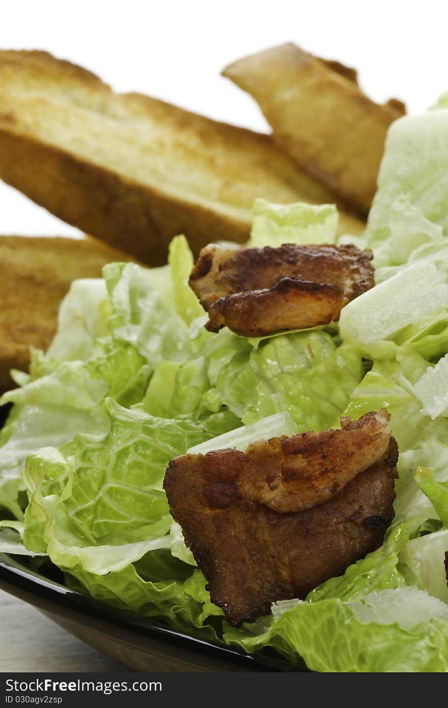 Somebody eating a fresh caesar salad in a plate with big piece of bacon on it. Very shallow depth of field. Somebody eating a fresh caesar salad in a plate with big piece of bacon on it. Very shallow depth of field.