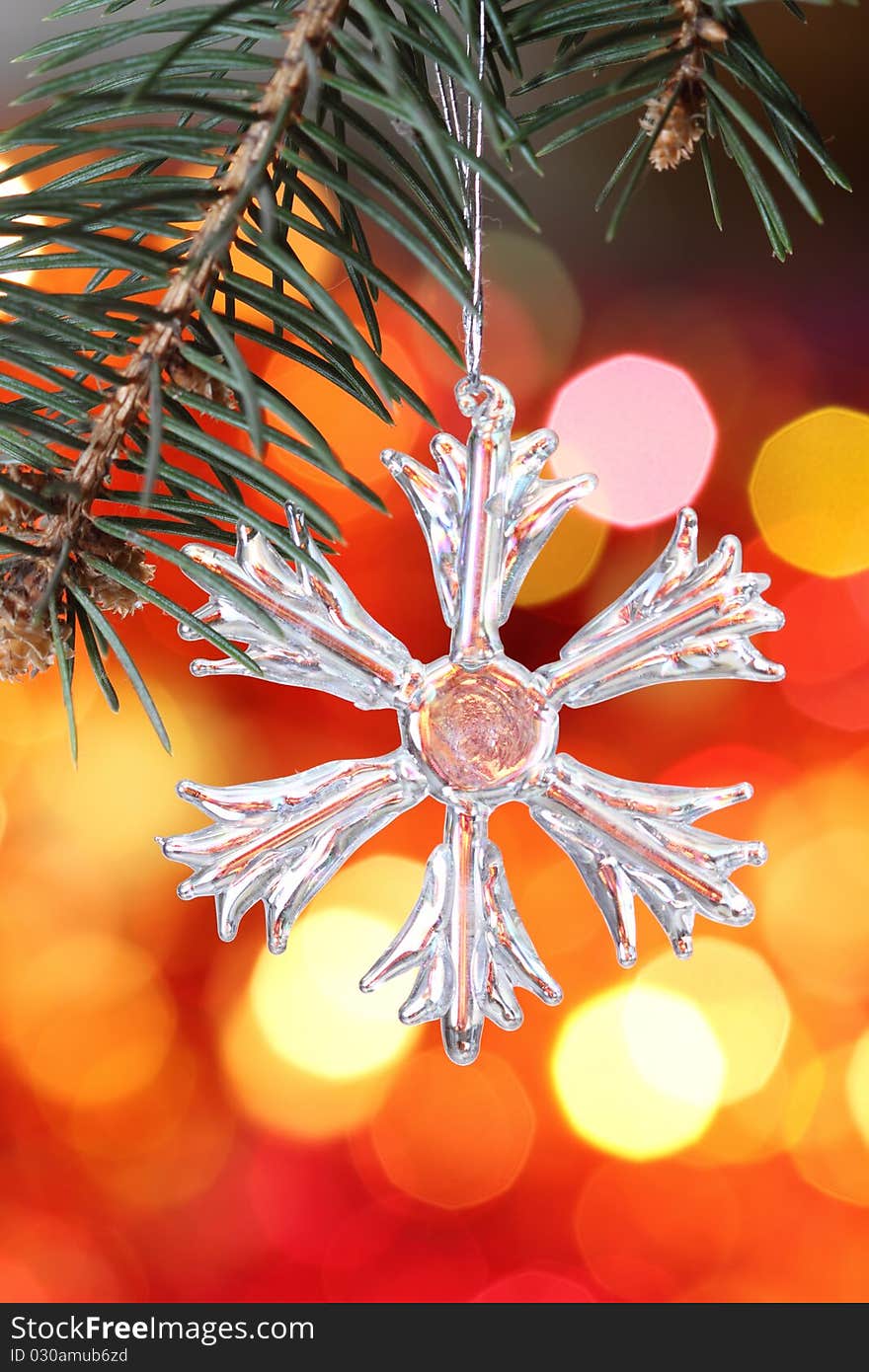 Snowflake on branch of Christmas tree against red blurred background