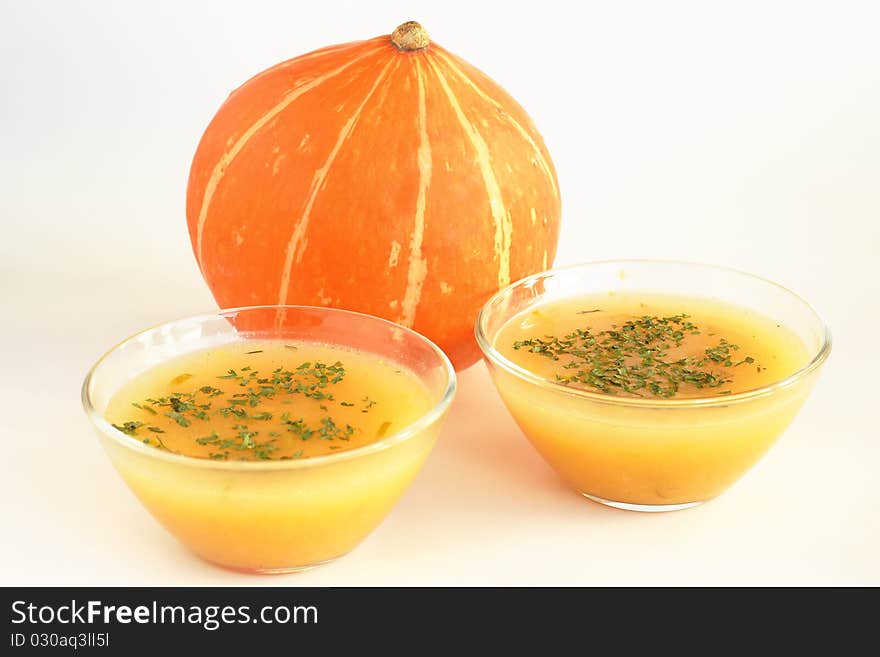 Two bowls of hot pumpkin soup and pumpkin on white