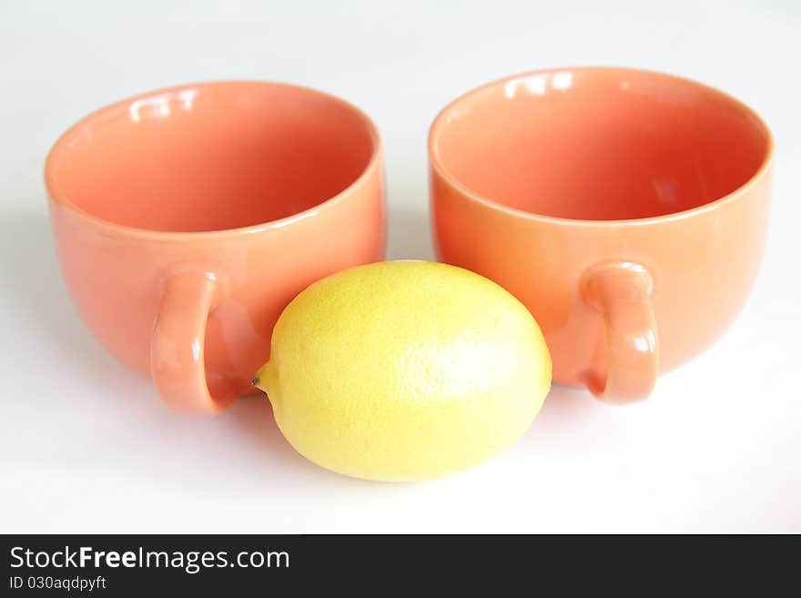 Two orange empty tea cups with whole lemon on white background. Two orange empty tea cups with whole lemon on white background