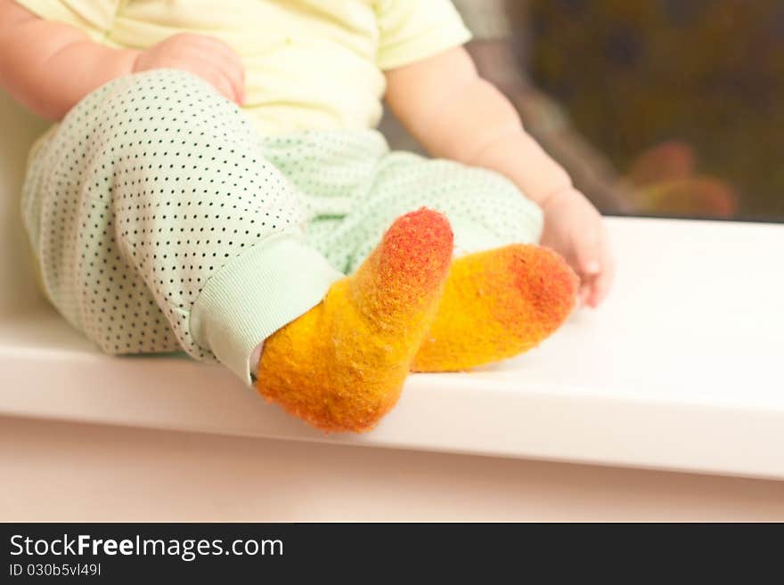 Adorable toddler girl sitting on the window sill, legs closeup. Adorable toddler girl sitting on the window sill, legs closeup