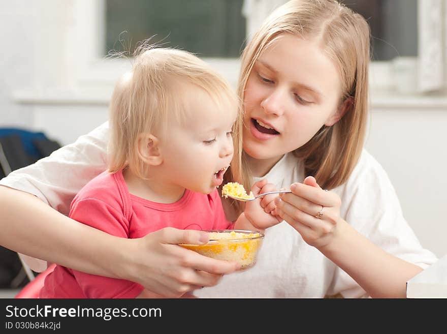 Mother feeding his daughter with porridge