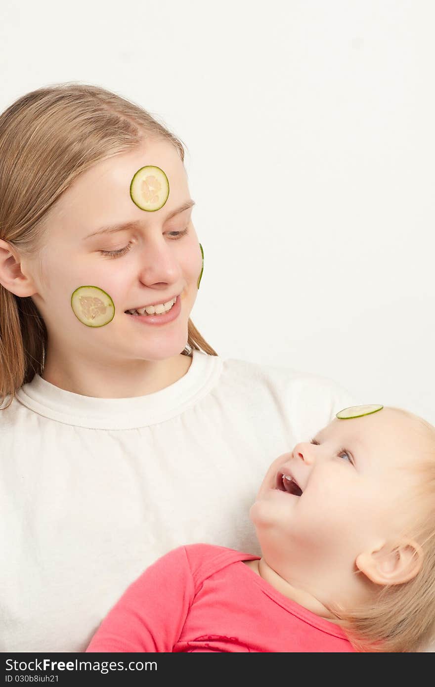 Young adorable mother with daughter play with sliced cucumbers on faces. Young adorable mother with daughter play with sliced cucumbers on faces