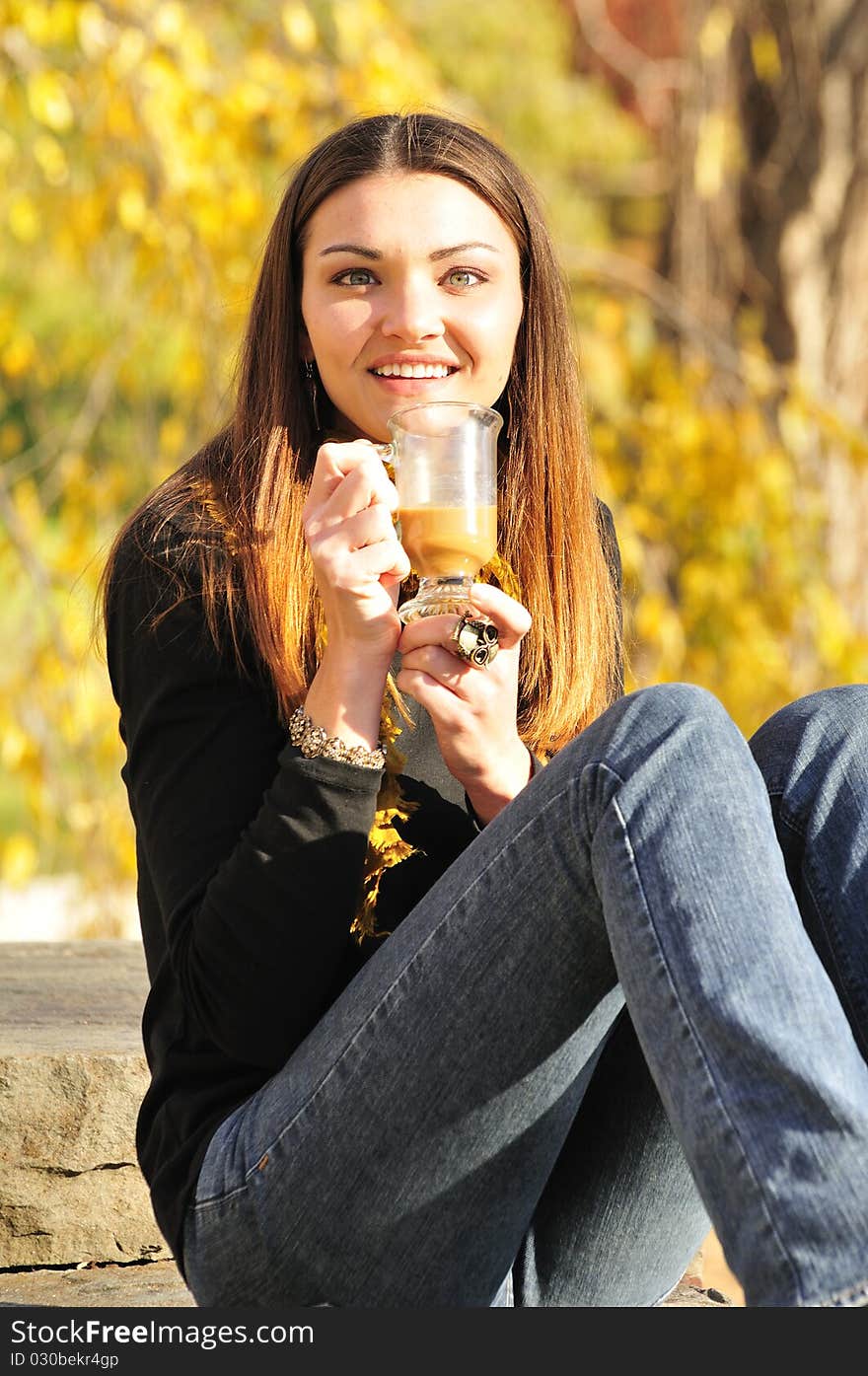 Happy young woman drinking coffee on a bright fall day