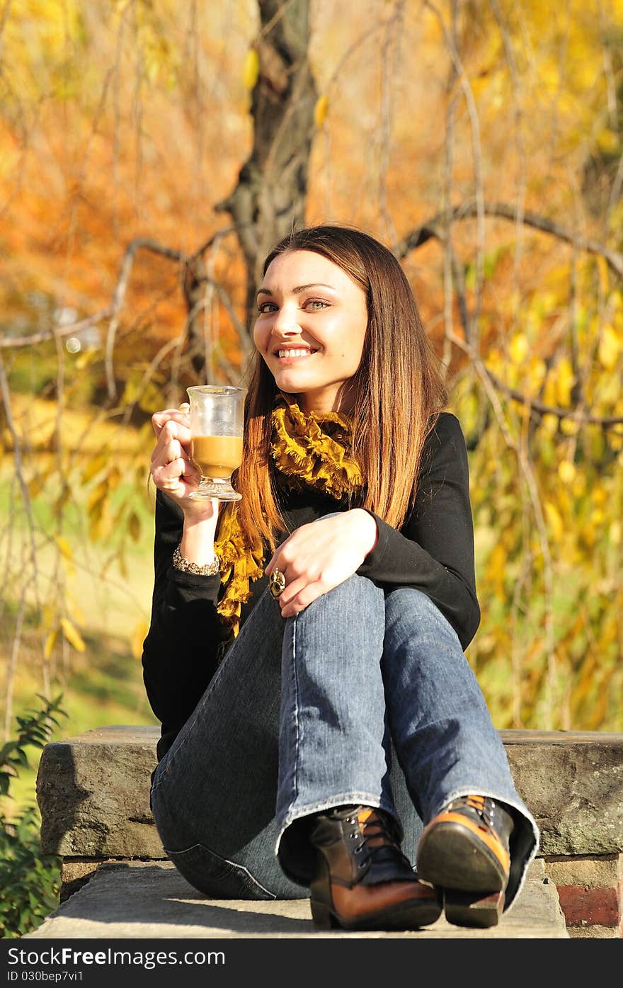 Happy young woman drinking coffee on a bright fall day