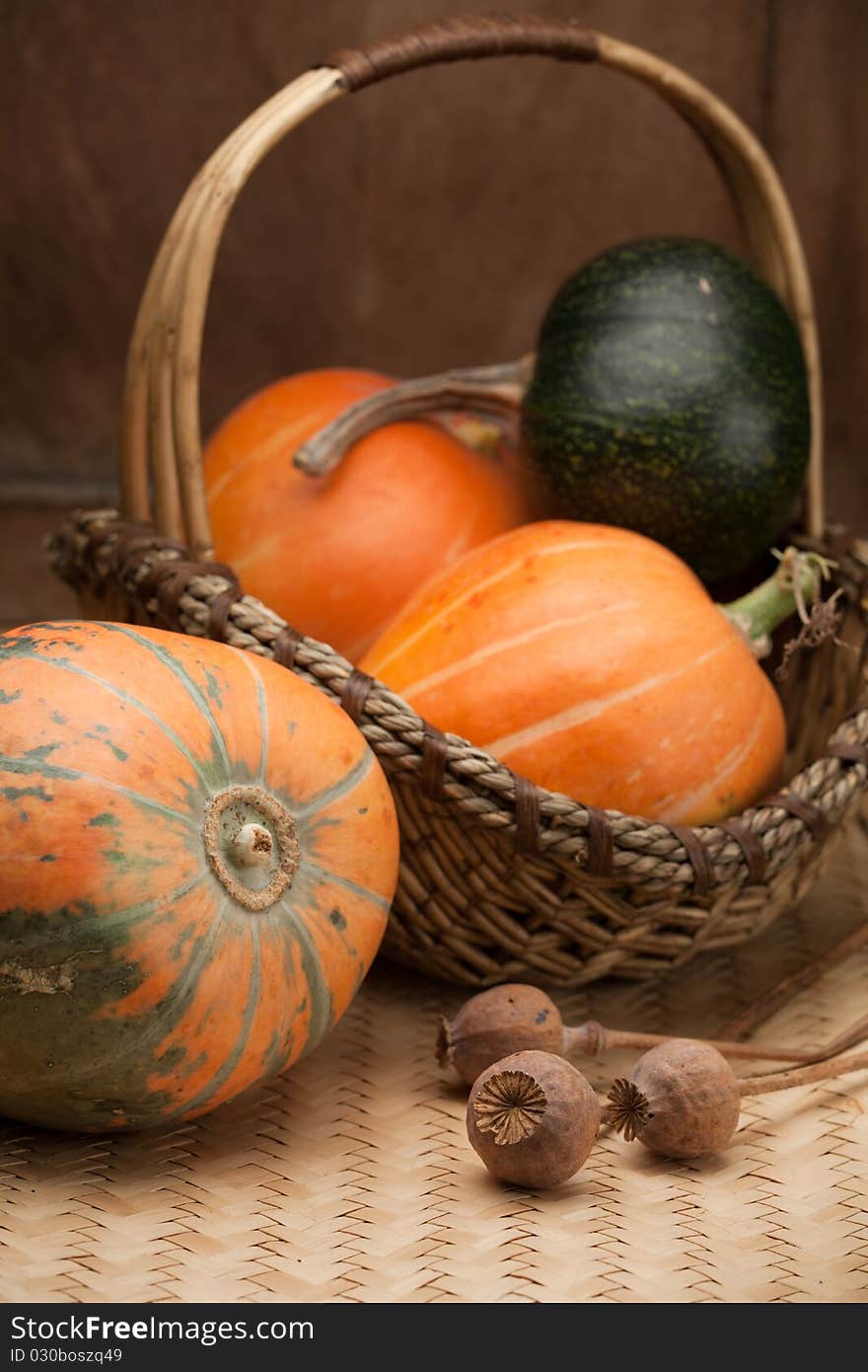 Ripe orange pumpkins in rural woven basket and poppy heads on wooden table. Ripe orange pumpkins in rural woven basket and poppy heads on wooden table