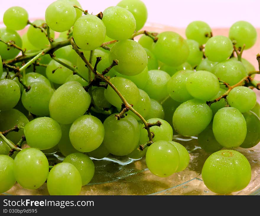 Clusters of green grapes, sitting on a glass plate, sitting on a wooden cutting board with a white background.