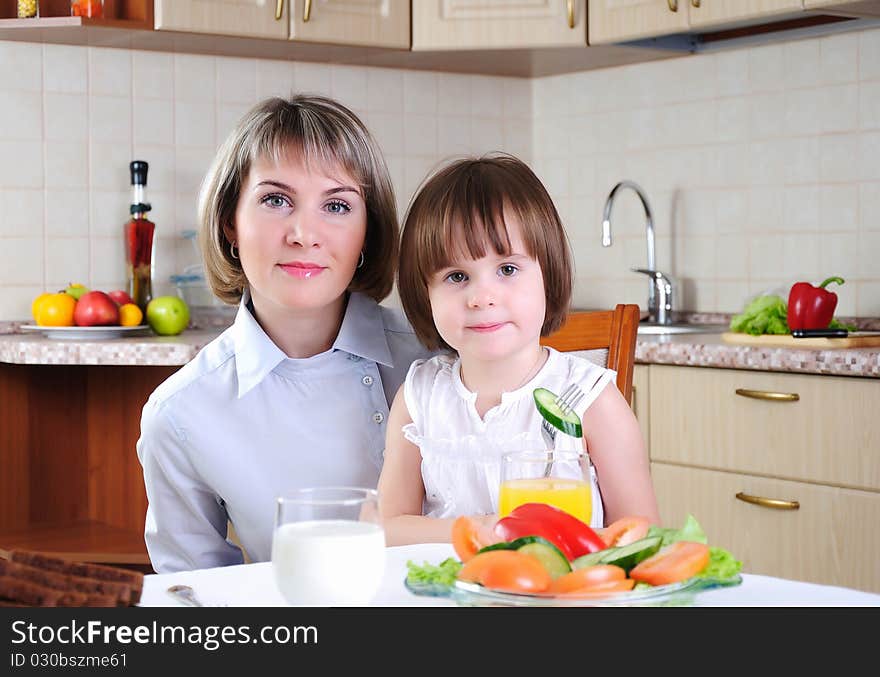 Mama and her little daughter eating breakfast in the morning together in the kitchen.