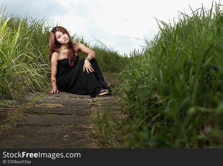 Asian woman sitting outdoor in the meadow with black dress. Asian woman sitting outdoor in the meadow with black dress