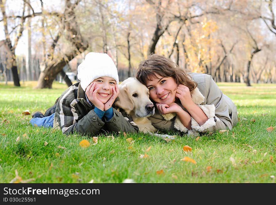 Mother and son together having fun in the autumn park playing with a golden retriever.