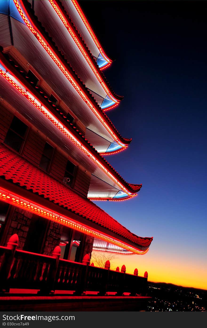 A view of a Chinese pagoda at dusk with the sunsetting over a city in the background. A view of a Chinese pagoda at dusk with the sunsetting over a city in the background