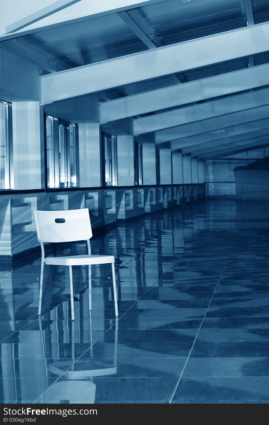 One white plastic chair standing in big hallway. Blue tone. One white plastic chair standing in big hallway. Blue tone