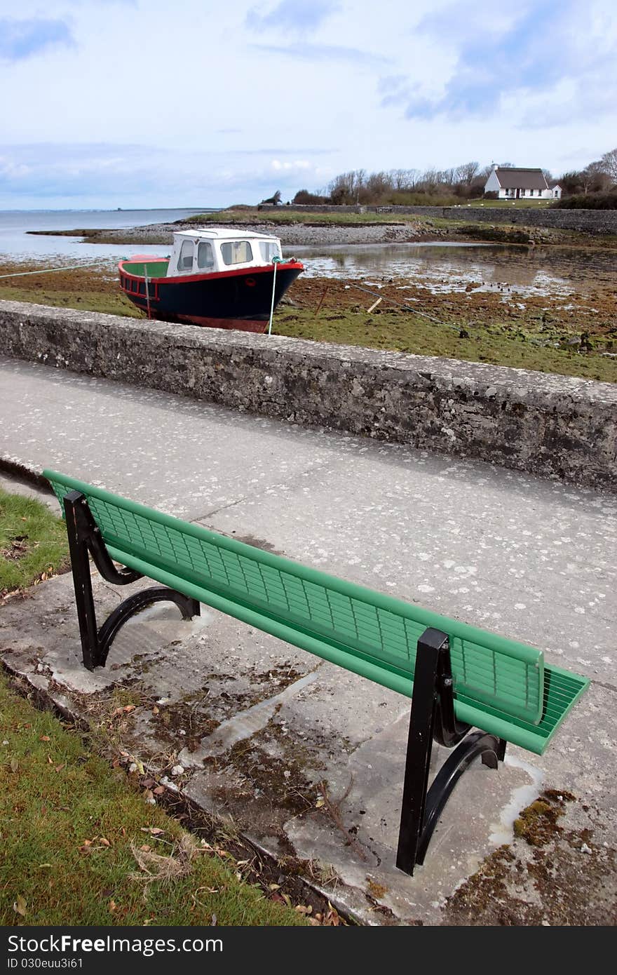 A green metal bech with a view of an old boat in a bay in ireland. A green metal bech with a view of an old boat in a bay in ireland