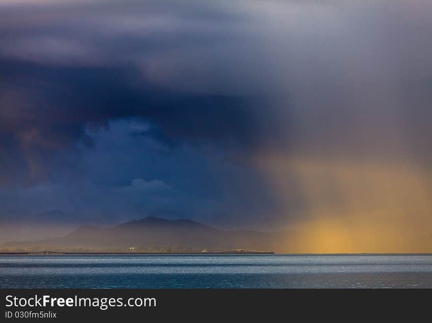 Thunder storm with rain lit by the sun at a lake