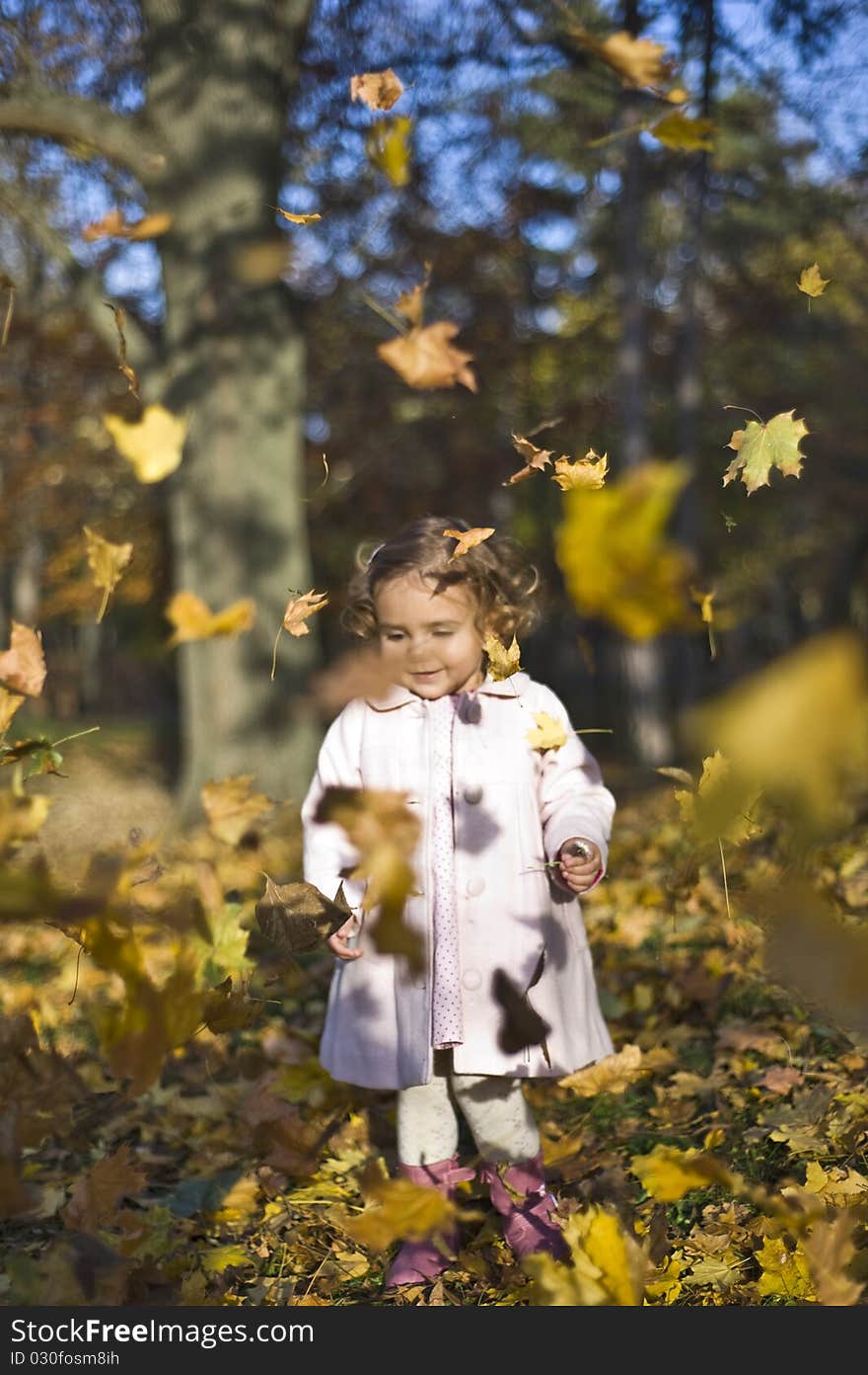 Portrait with little girl in autumn in the park with leaves fallen down on her