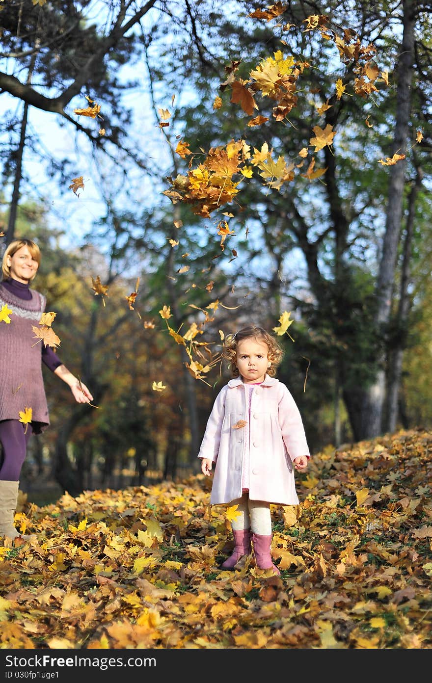 Portrait with little girl in autumn in the park with leaves fallen down on her and mom in the background