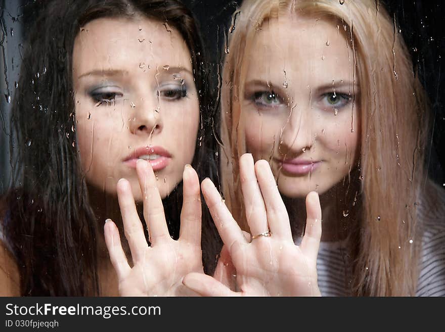 Two young girls behind wet window. Two young girls behind wet window