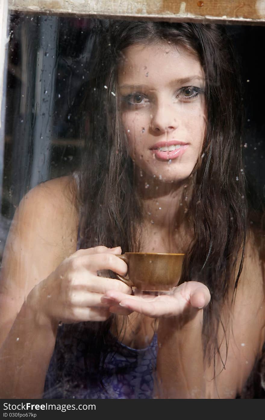 Young girl with cup of tea behind wet window