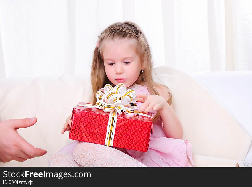 A little girl give a holiday gift in red box with white ribbon.