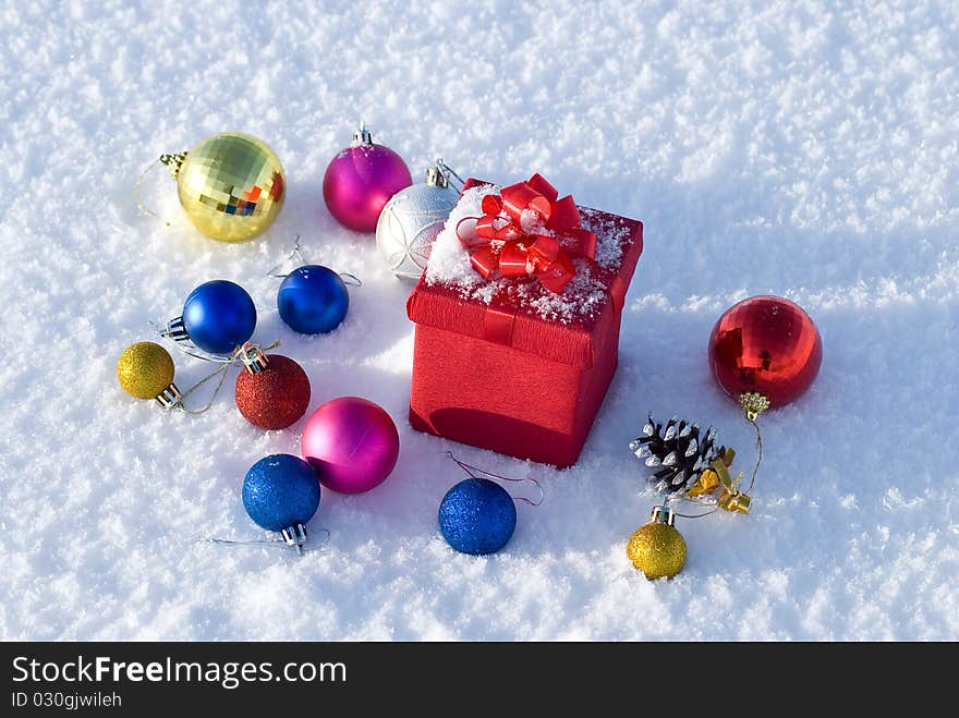 Red gift box on snow with christmas balls