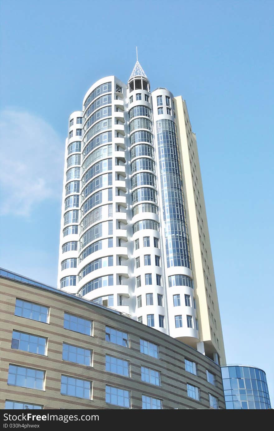 The modern habitant building of many storeys stays against blue sky. It loos like high tower directed to sky. View from below. There is harmony between white building and light blue sky with fleecy clouds. The modern habitant building of many storeys stays against blue sky. It loos like high tower directed to sky. View from below. There is harmony between white building and light blue sky with fleecy clouds.