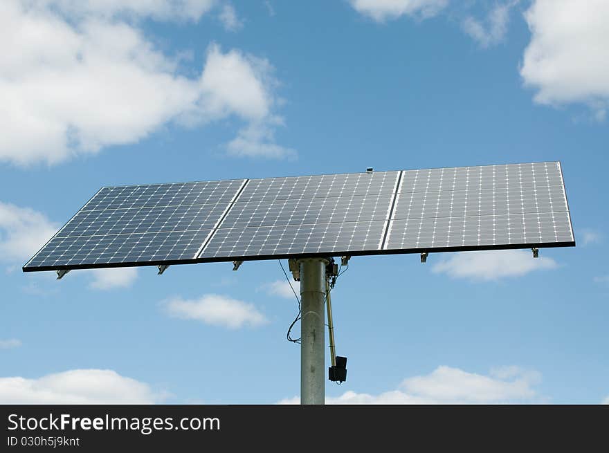 A modern photovoltaic solar panel array generates electricity with blue sky and clouds in the background. A modern photovoltaic solar panel array generates electricity with blue sky and clouds in the background.