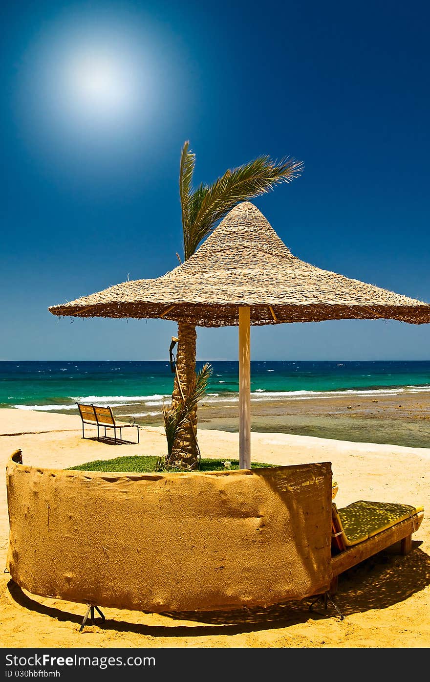 Palm, bench, parasol and sea against blue sky. Palm, bench, parasol and sea against blue sky.