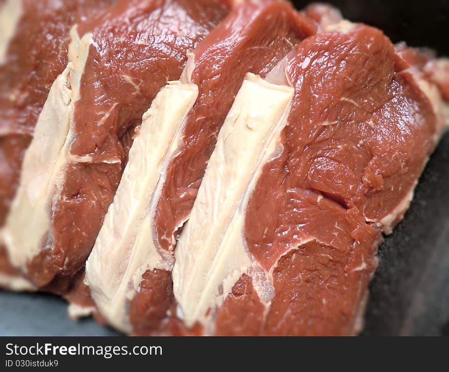 Four raw bloody beef steak slices.