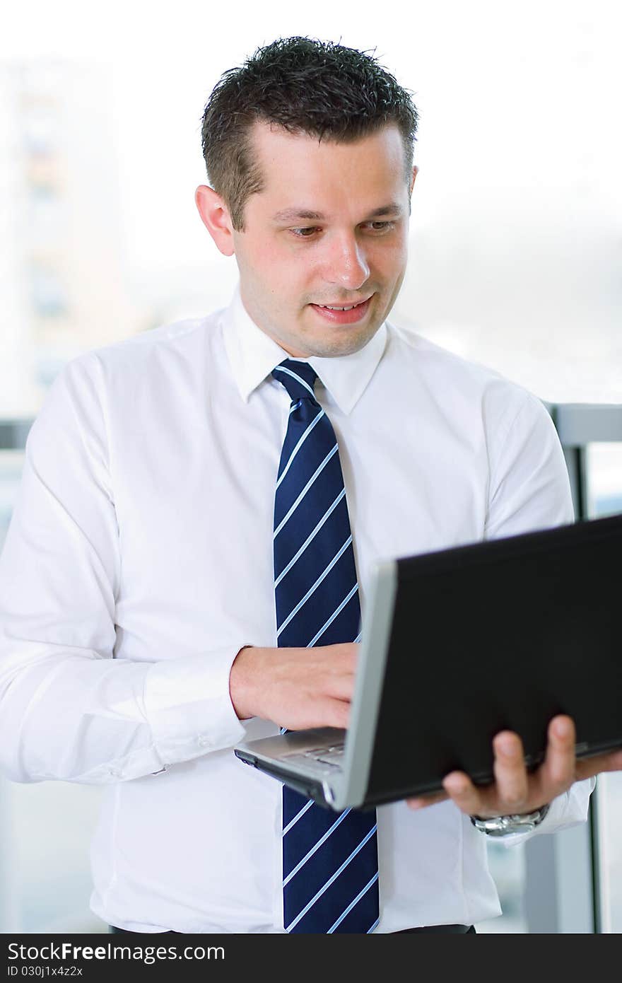 Casual looking businessman working on laptop computer in front of office window.