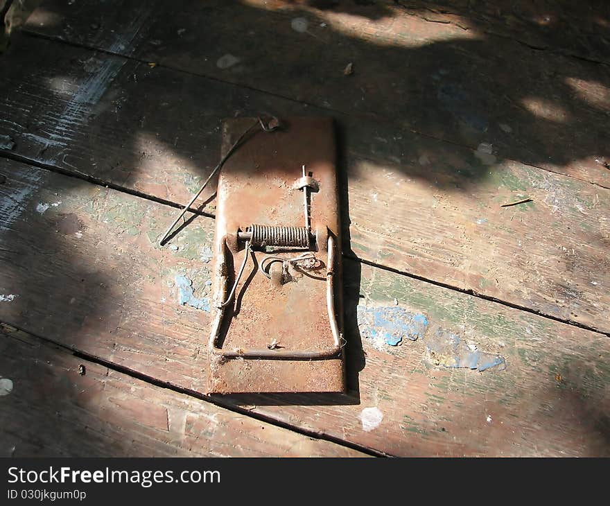 Rusty mousetrap on boards with scratches, at a sunlight in a shade