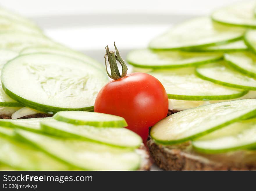 Small red tomato among pieces of rye bread with sliced cucumbers and cheese. Small red tomato among pieces of rye bread with sliced cucumbers and cheese