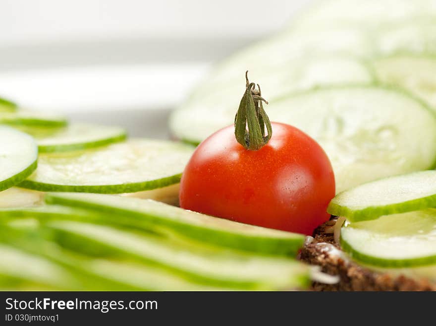 Small red tomato among pieces of rye bread with sliced cucumbers and cheese. Small red tomato among pieces of rye bread with sliced cucumbers and cheese