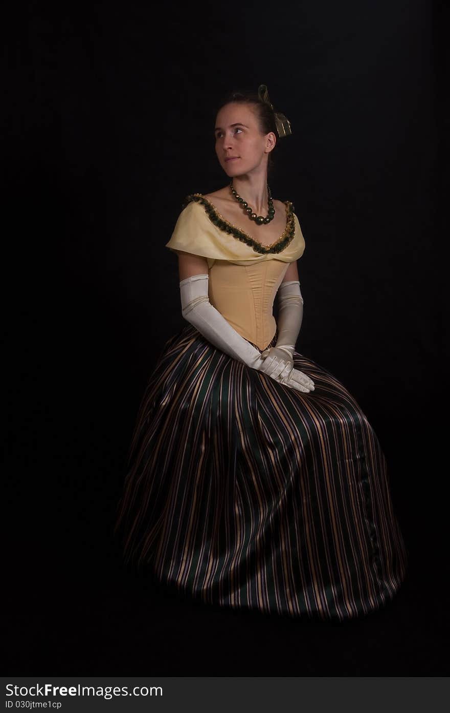 Sitting girl in nineteenth century dress isolated on black