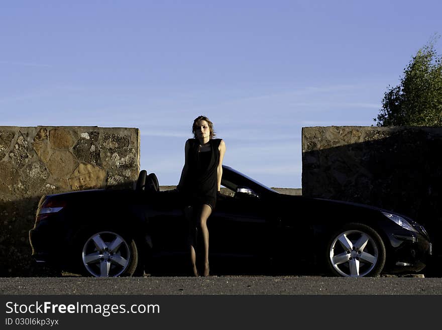 View of a beautiful woman next to sports car on a fashion pose. View of a beautiful woman next to sports car on a fashion pose.