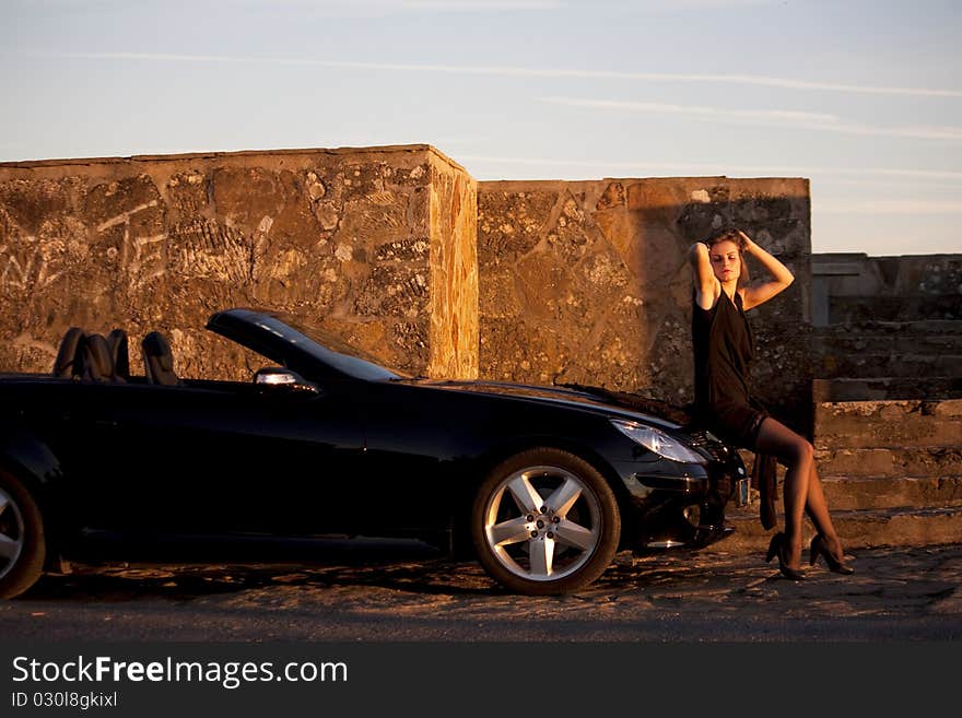 View of a beautiful woman next to sports car on a fashion pose. View of a beautiful woman next to sports car on a fashion pose.