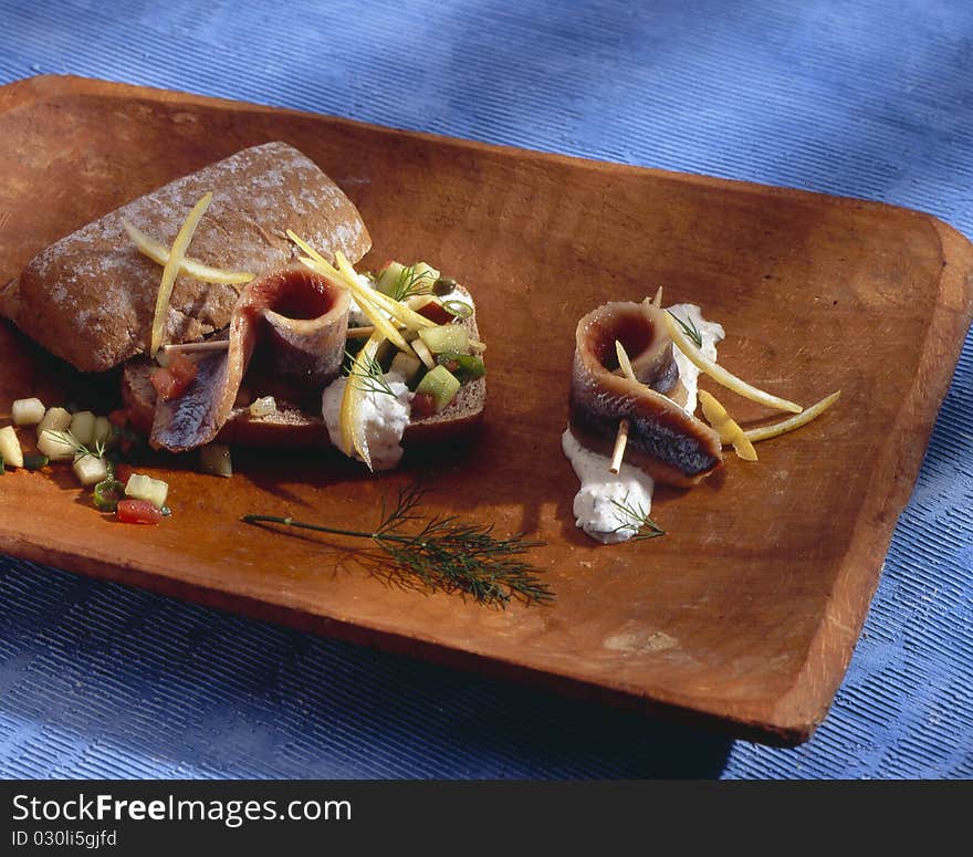 Matjes is a salted herring, here with bread on a wooden plate on a blue underground