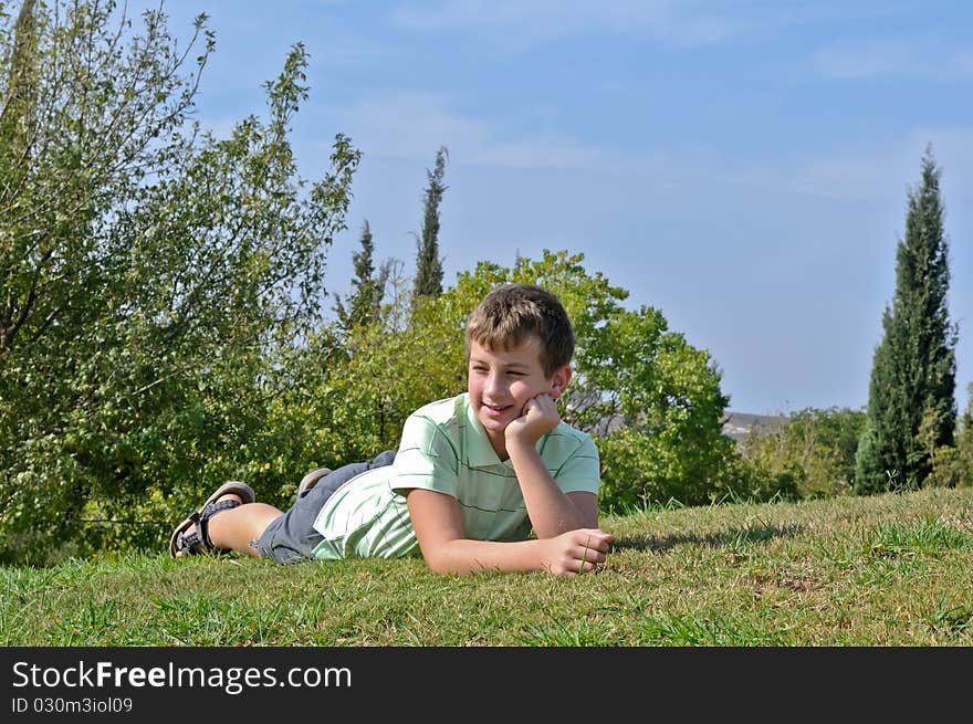 Portrait of a boy lying on the grass in the park and sustaining head on his hand. Portrait of a boy lying on the grass in the park and sustaining head on his hand