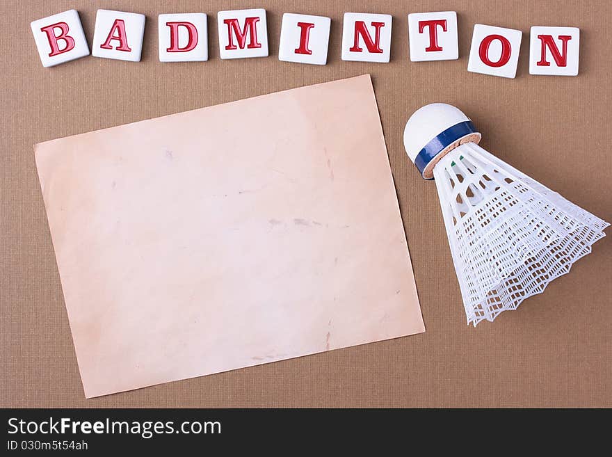 A white synthetic badminton shuttlecock next to a piece of paper. Add your text to the paper.