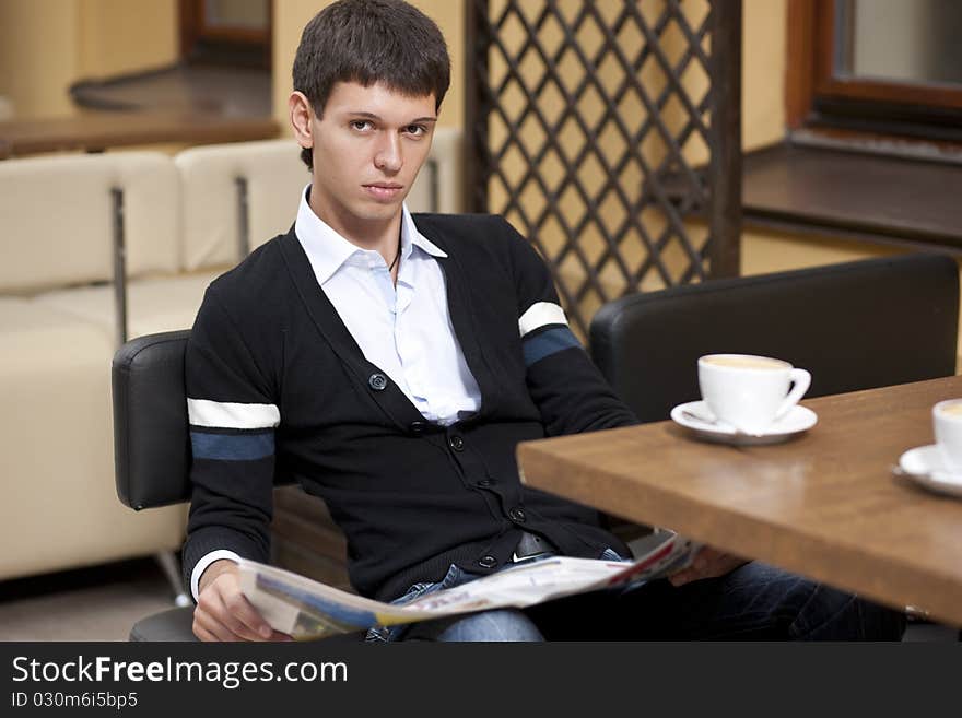 Young man with newspaper posing for camera across table with cup of coffee. Young man with newspaper posing for camera across table with cup of coffee